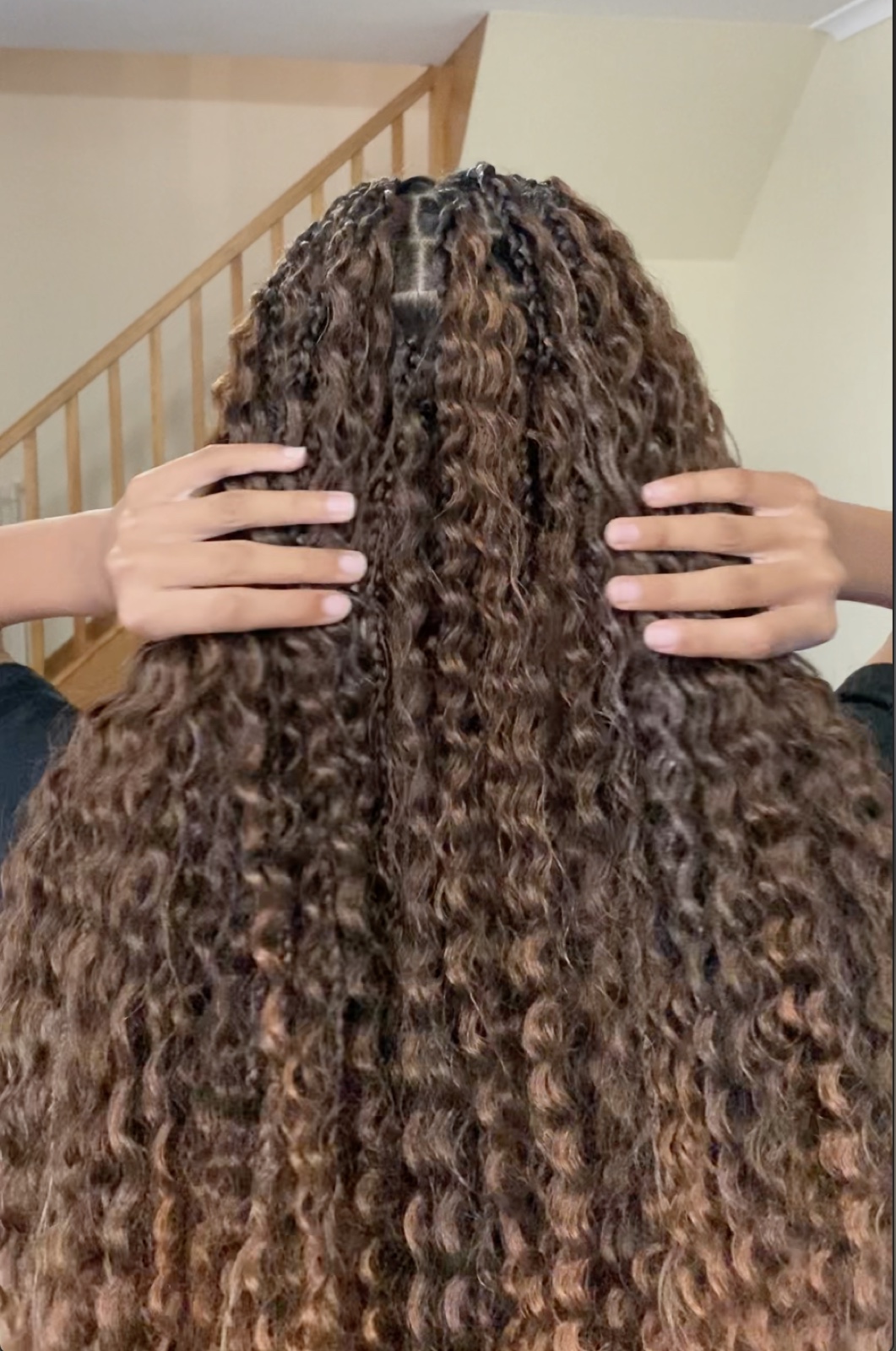 Back view of long boho braids with curly cascading ends, the client's hands resting in the hair.