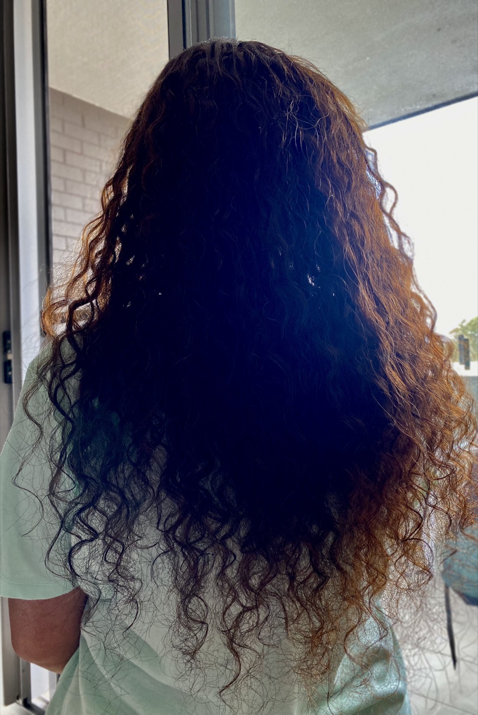 A finished sew-in install with long flowing curls, back view.